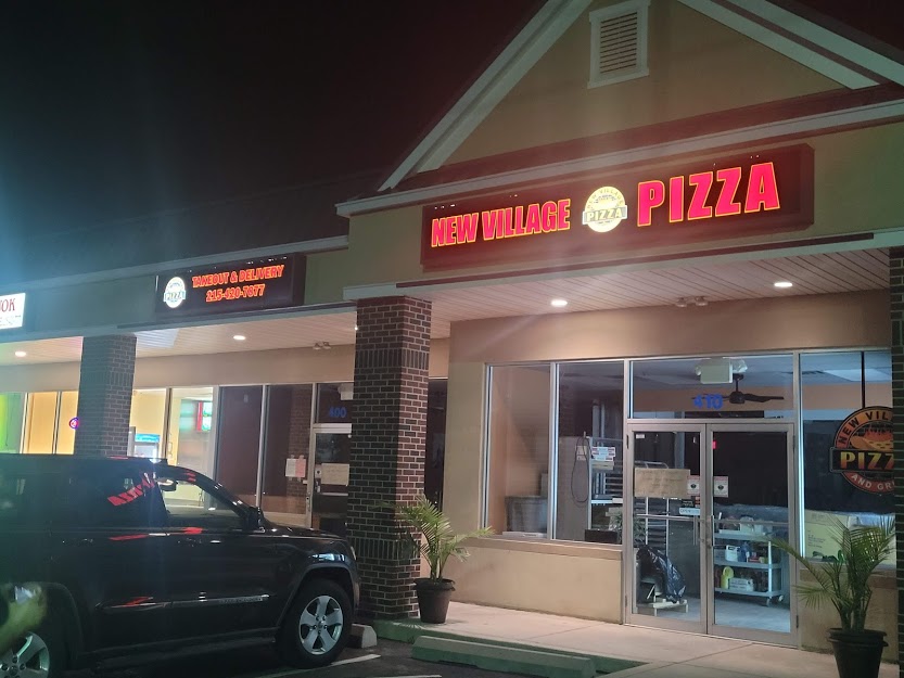 A pizza restaurant at night with cars parked outside.